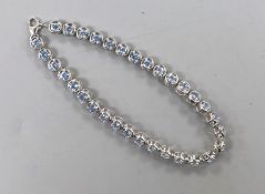 A modern 375 white metal and blue topaz line bracelet, 20cm, set with thirty two stones, gross