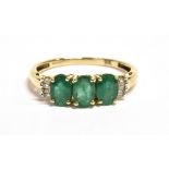 A 9CT GOLD EMERALD AND DIAMOND DRESS RING the ring set with three facetted oval emeralds with