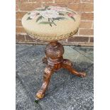 AN EDWARDIAN REVOLVIING PIANO STOOL with tapestry upholstered circular seat on carved tripod base,