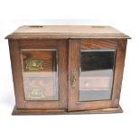 AN OAK SMOKERS CABINET with hinged top and glazed doors opening to interior fitted with drawers