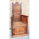 A LARGE OAK ARMCHAIR WITH HIGH BACK and cupboard beneath the solid seat, 68cm wide across arms,