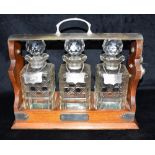 AN EP MOUNTED OAK FRAMED THREE DECANTER TANTALUS the three cut glass decanters with plated labels