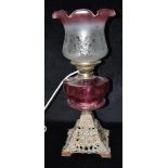 AN EDWARDIAN OIL LAMP CONVERTED TO ELECTRICITY with cranberry glass reservoir and shade with