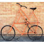 A CIRCUS BICYCLE painted orange, with a high frame and rear foot step/rest, the wheels 61cm (24