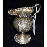 A GEORGE III SMALL SILVER JUG The jug on a pedestal base and embossed with flora and a vacant