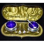 A CASED PAIR OF SILVER CONDIMENTS with blue glass liners hallmarked for Chester 1916, together
