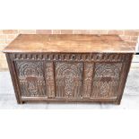 A CARVED OAK COFFER the lid with chip carved decoration, three panel front with arcade carved