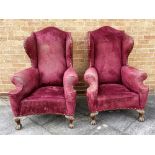 A PAIR OF LARGE UPHOLSTERED WING ARMCHAIRS with camel backs and outscrolled arms, on claw and ball
