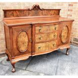 A SHAPED FRONT MAHOGANY AND BURR WALNUT SIDEBOARD fitted with three drawers flanked by cupboards, on