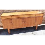 A TEAK SIDEBOARD fitted with four drawers with recessed pull handles above four drawers, on tapering