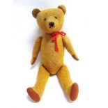 A GOLD MOHAIR TEDDY BEAR with pale orange glass eyes and a black horizontally stitched nose, on a