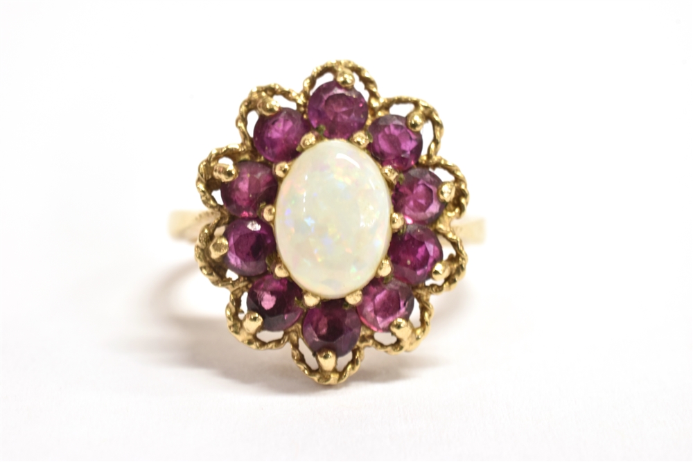 A 9CT GOLD PINFIRE OPAL AND GARNET GLASS FLOWER HEAD RING The central oval opal measuring 0.7cm x