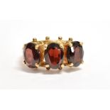 A 9CT GOLD GARNET GLASS THREE STONE DRESS RING The stones measuring 0.8cm x 0.5cm, the shank