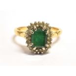 AN 18CT GOLD EMERALD CLUSTER RING The step cut Emerald measuring approx. 6 x 5mm and surrounded by