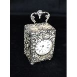A SILVER CARRIAGE CLOCK The case with heavily embossed scroll fancy pattern, scroll handle and