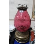 A large church oil/heater lamp with squat brass base fount and a cranberry glass shade in a