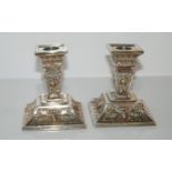 A pair of silver dwarf candlesticks with fixed sconces on square tapering stems with foliate