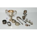 A lot comprising a silver trophy cup, rubbed marks 12 cm high, silver sugar tongs, two silver napkin