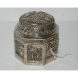A Burmese octagonal box with hinged cover, embossed with figures, buildings and trees, 10cm high,