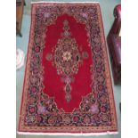 A red ground fine Keshan rug with blue central medallion, spandrels and borders, 225cm x 129cm