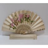 A cream silk fan painted with pink roses, with mother of pearl handle, with metallic decoration