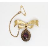 A 9ct gold bow brooch with a yellow metal garnet set locket back pendant attached, weight 4.3gms