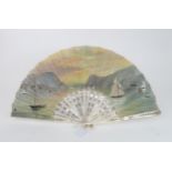 A LARGE PAINTED FAN the gauze leaf painted with a scene of boats in a sunset harbour, mounted on