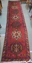 A red ground Heriz runner with geometric medallions and multicoloured border, 381cm long x 88cm wide