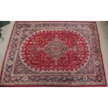 A RED GROUND KESHAN RUG with blue central medallion, matching spandrels and borders, signature to