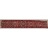 A RED GROUND HERIZ RUNNER with geometric medallions, 394cm long x 64cm wide Condition Report: