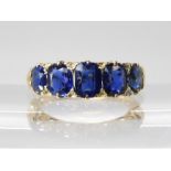 A FIVE SAPPHIRE RING in a classic yellow metal scrolled mount. Largest sapphire measures approx 5.