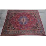 A RED GROUND PERSIAN HAND KNOTTED MASHAD RUG with cream and blue central medallion, matching blue