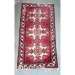 A red ground Persian rug with three geometric medallions and cream borders, 191cm long x 104cm