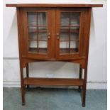 A 20th century mahogany arts and crafts style two door glazed bookcase on square supports