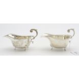 A pair of George VI silver sauceboats, with rococo style flying scroll handles, on three hoof