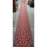 A red ground Axminster style runner with all over floral design and dark blue borders, 790cm high