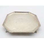 A silver card tray, of octagonal form, with engraved presentational inscription, on four bracket paw
