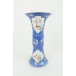A CHINESE GU VASE painted with leaf shaped panels of foliage reserved on a blue foliate incised