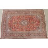 A RED GROUND KESHAN RUG with all over floral foliate design, dark blue central medallion, matching