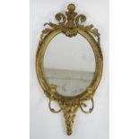 A 19TH CENTURY GILT AND GESSO OVAL GIRANDOLE WALL MIRROR  with two branch candle holder and floral