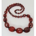 A string of faceted cherry amber coloured beads, dimensions of largest bead 3cm x 2.2cm, length