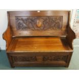 An early 20th century oak monks bench/settle with carved back over hinged seat on base carved with