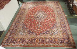 A red ground Kashan wool rug with a blue and cream central medallion, matching spandrels and a