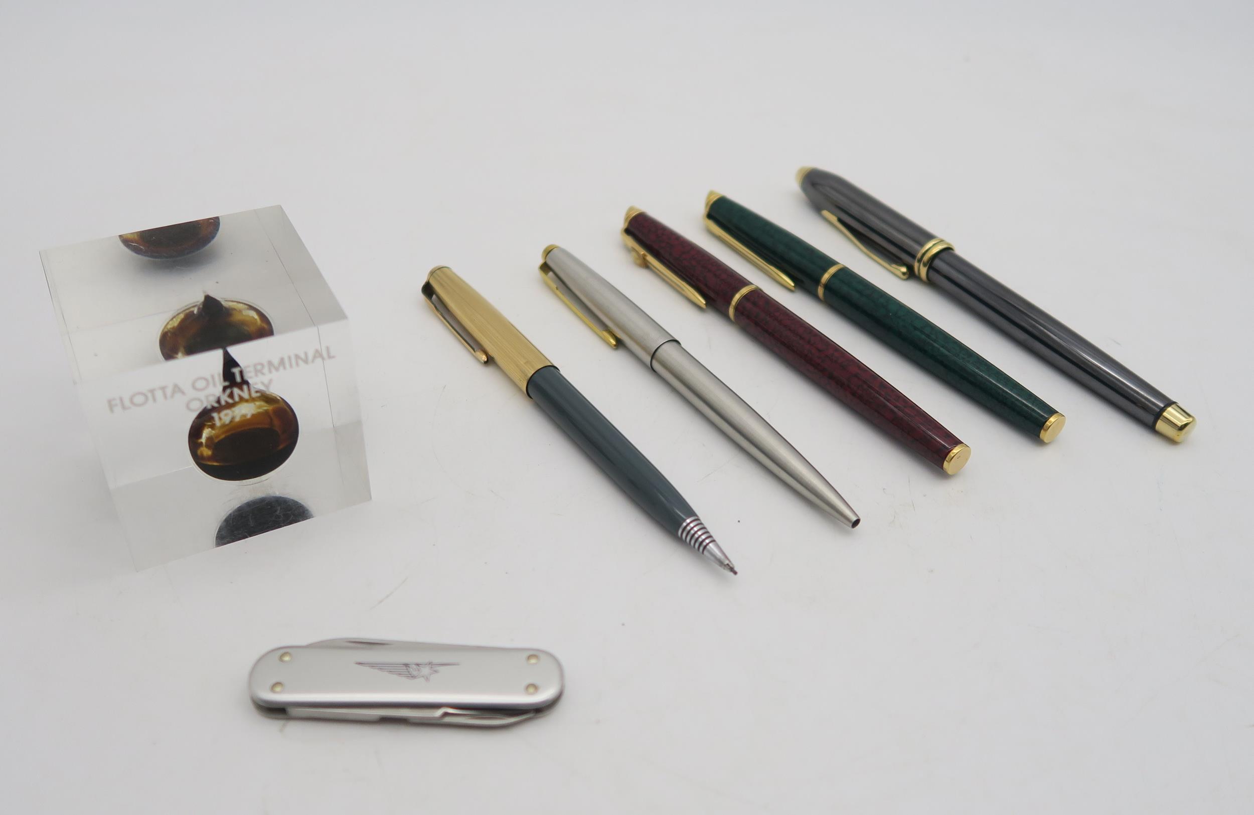 Five various pens comprising Cross, Waterman and Parker; a Perspex paperweight containing crude