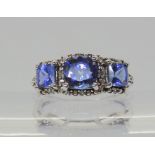 A 9ct white gold three stone cushion cut tanzanite ring with diamond accents, finger size J1/2,