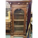 A Victorian oak glazed display cabinet extensively carved with lion masques, cherubs and fruit on