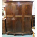An early 20th century mahogany bow fronted three door wardrobe with moulded dentil cornice over