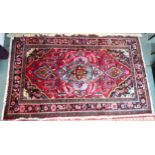 A red ground Kashan rug with blue central medallion, black spandrels and multicoloured floral