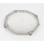 AN EDWARDIAN SILVER SALVER of plain form, with a gadrooned shellwork border, on four scroll feet, by