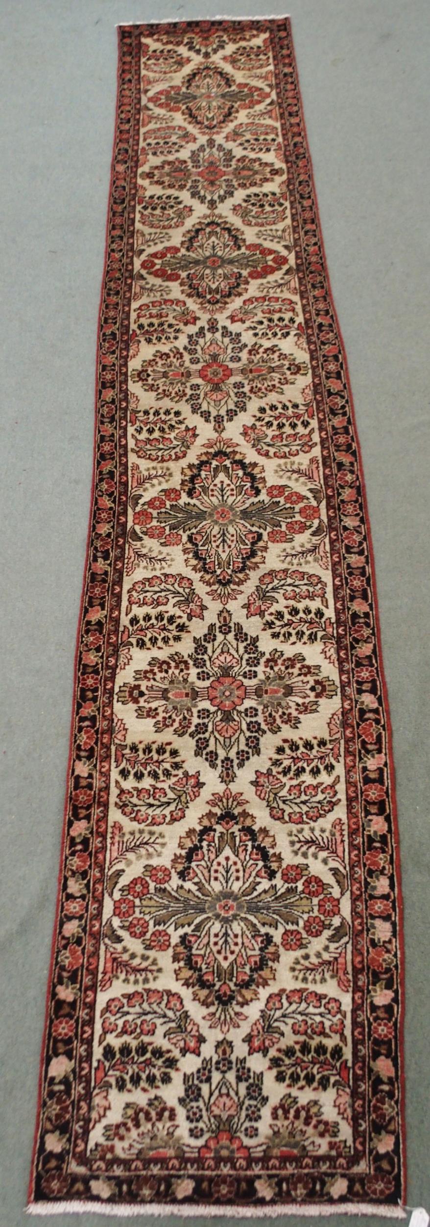 A CREAM GROUND HAMADAN RUNNER with seven floral medallions and dark blue floral border, 459cm long x